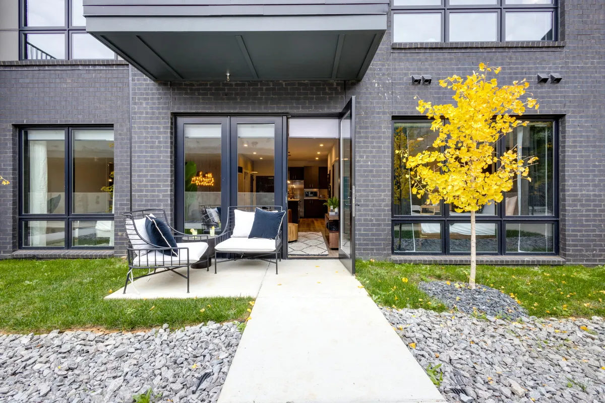 A stylish private patio area with comfortable seating, set against the backdrop of modern architecture and a yellow tree. The space is inviting and ideal for relaxing outdoors or enjoying skyline views.