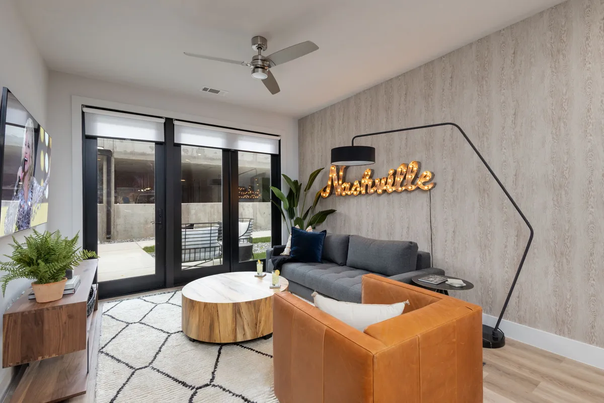 A welcoming living space with a prominent Nashville neon sign, a modern sofa, a round wooden coffee table, and expansive windows flooding the room with natural light. The decor is stylish and creatively nods to Music City.