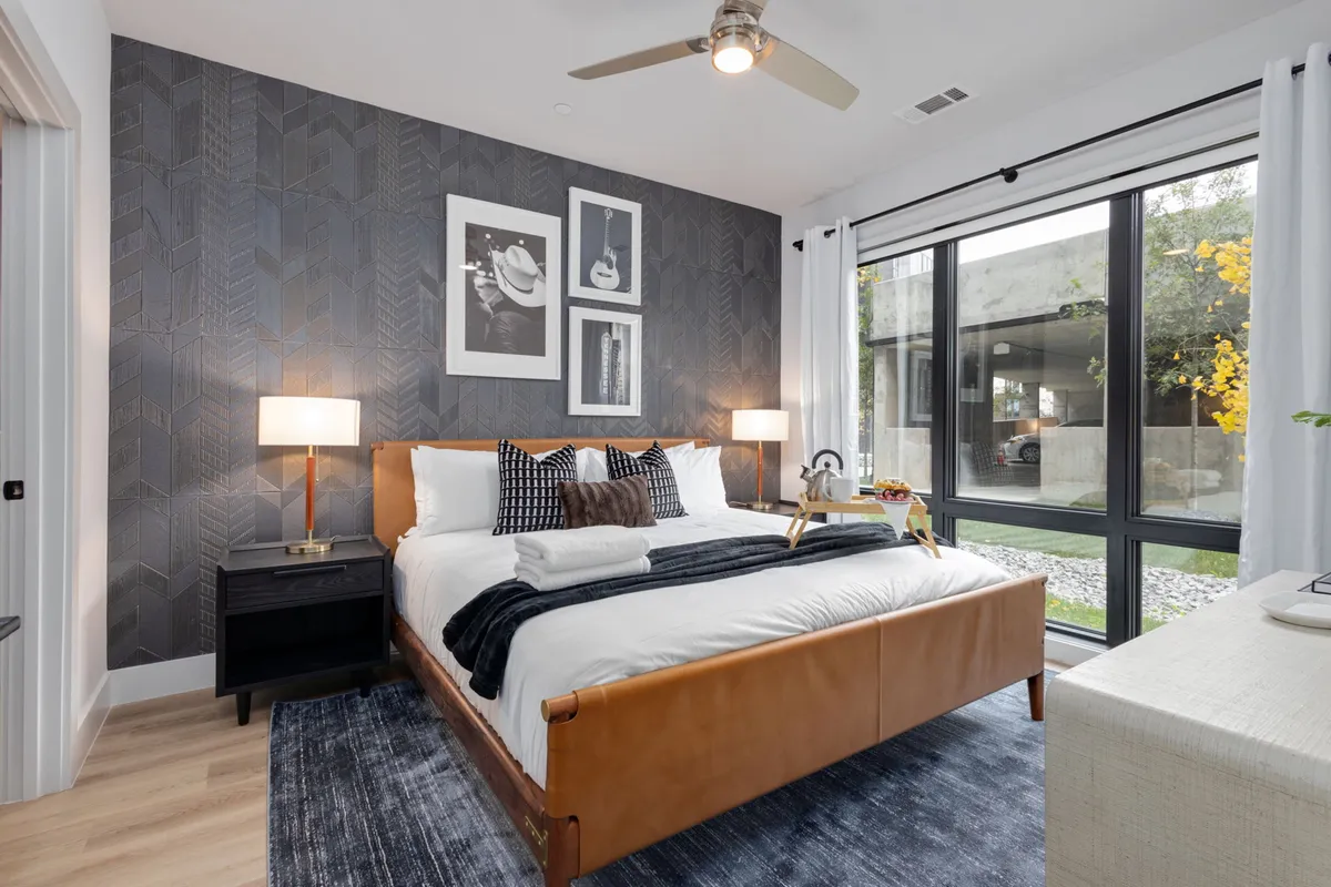 A serene bedroom with a comfortable bed, nightstands, a window allowing natural light, and modern artwork on the wall. The calm and uncluttered space is ideal for relaxing, reading, or enjoying a peaceful start to the day.