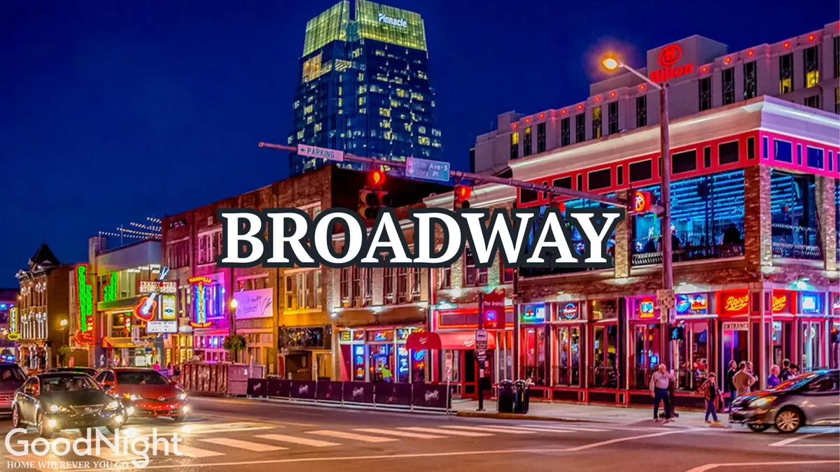 A bustling Nashville street comes alive after dark with neon-lit buildings, crowds of people, and vibrant nightlife. Diners enjoy meals, musicians perform live, and friends gather amongst the bright lights and energetic atmosphere characteristic of Broadway and downtown after sunset.