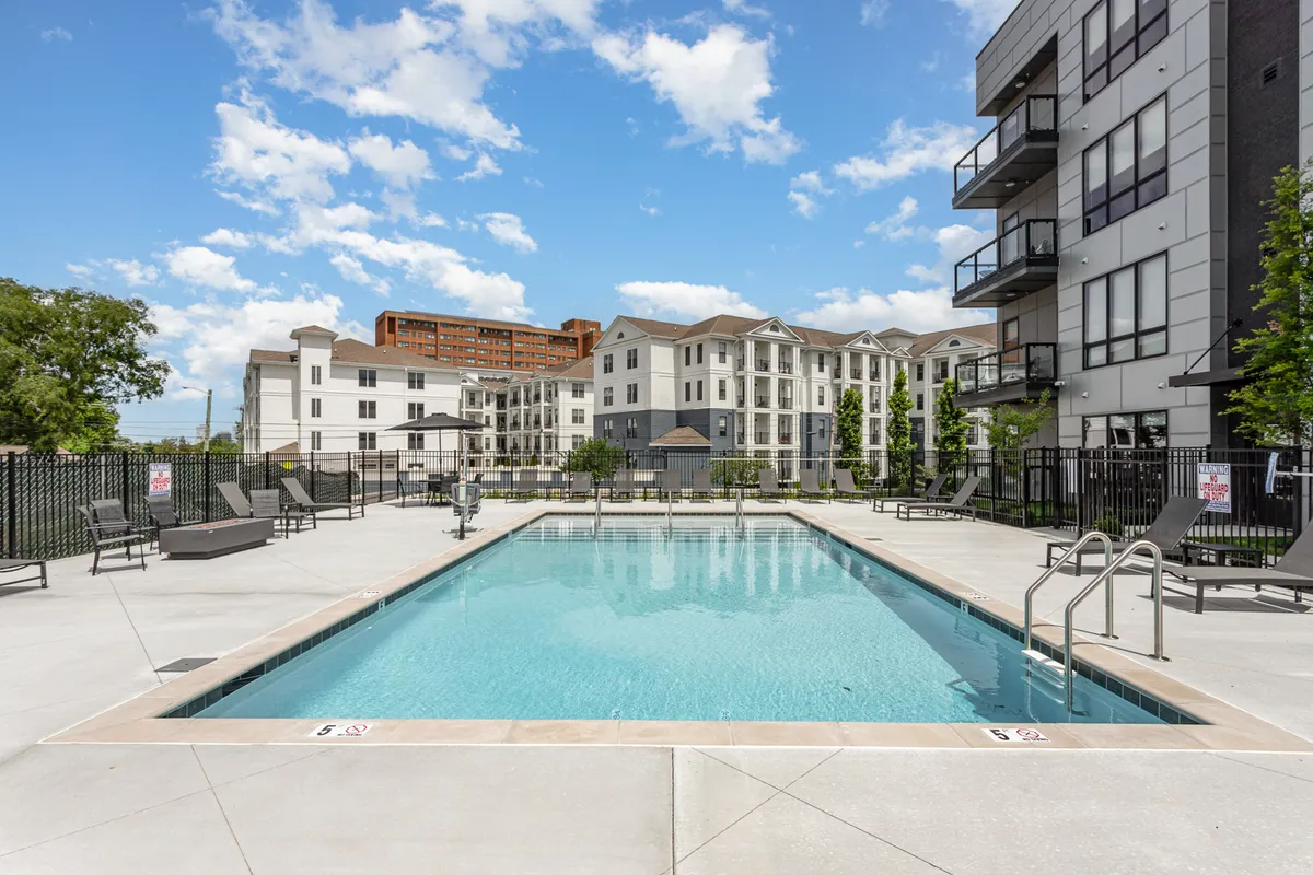 A sparkling swimming pool edged with lounge chairs is surrounded by the modern building's exterior. The relaxed setup offers a taste of the resort-style amenities available to families, with the inviting water suggesting year-round fun.