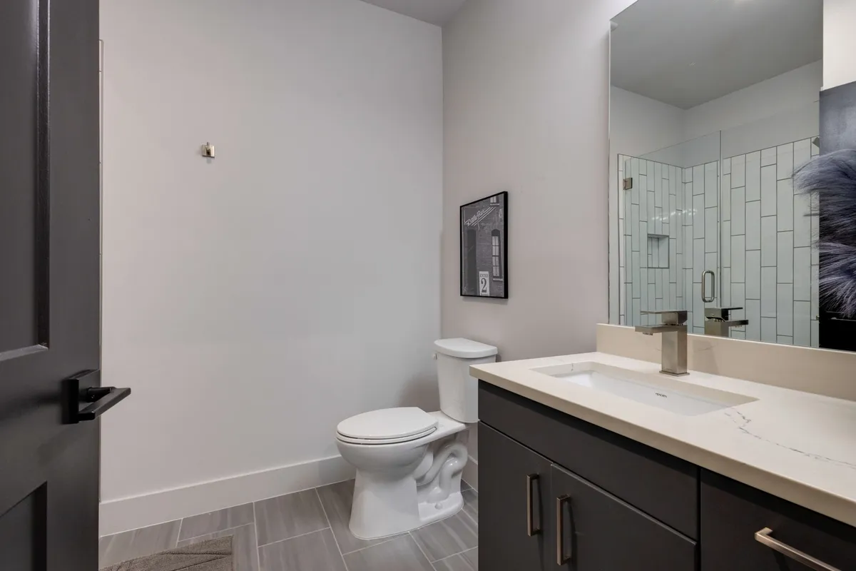 A contemporary bathroom with a vanity sink, large mirror, shower area, and toilet, all in a sleek, modern design. The space is bright and functional, perfect for refreshing after a day in the city.