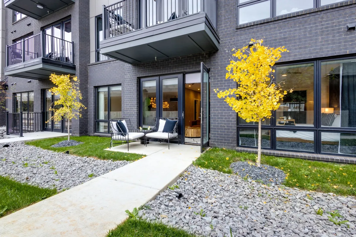 The hero image showcases the home's inviting exterior framed by vibrant yellow-leafed trees, highlighting a stylish outdoor seating area perfect for gatherings. Large glass windows reveal a warm interior, while the outdoor space hints at cozy evenings by the fire pit or peaceful mornings with coffee under the sunlight.